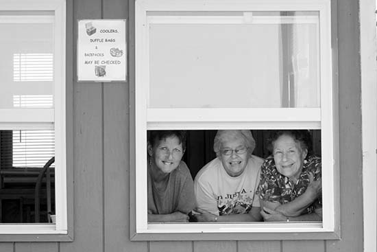 Three older women smile out of a window.