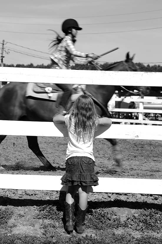 A little girl watches a horseback rider at a fair.