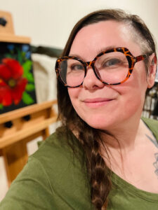 Headshot of Tilly. She is wearing a green sweater and large glasses