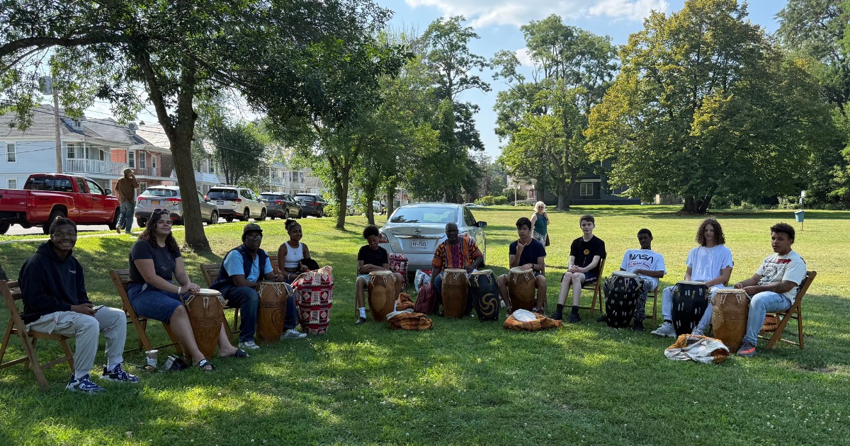A group of teenagers sit with drums between their legs in a semi circle. Zorkie Nelson sits directly in the middle